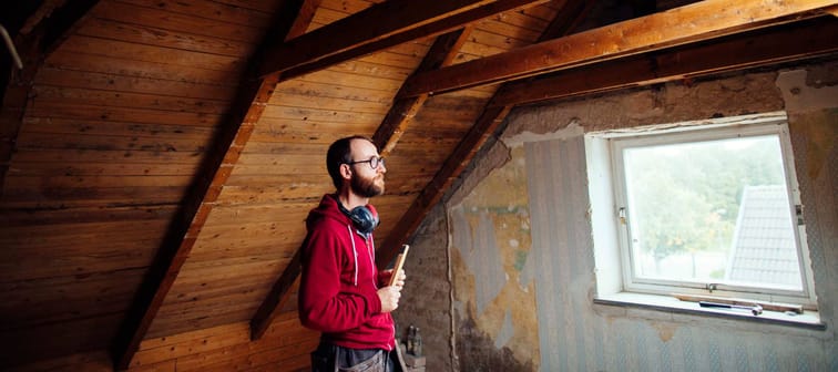 Man contemplating a renovation project in an attic space.
