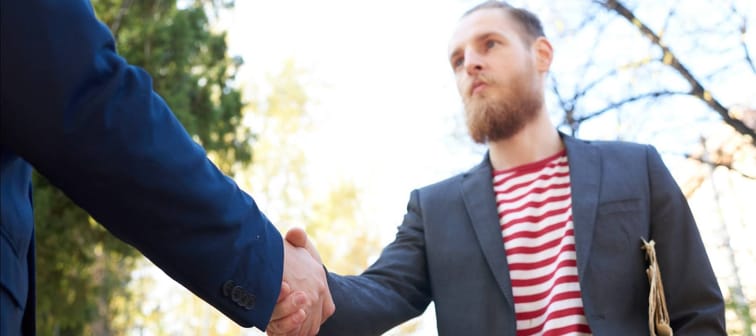 Low angle portrait of young bearded businessman shaking hands with unrecognizable partner outdoors meeting in park