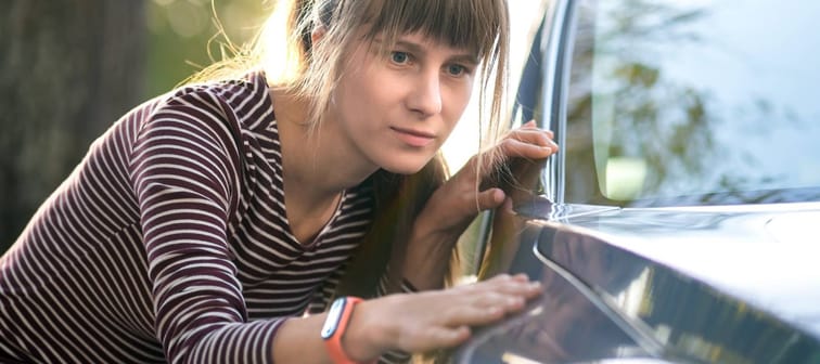 Young woman customer closely examining a new car at dealer outdoor shop before purchasing it.