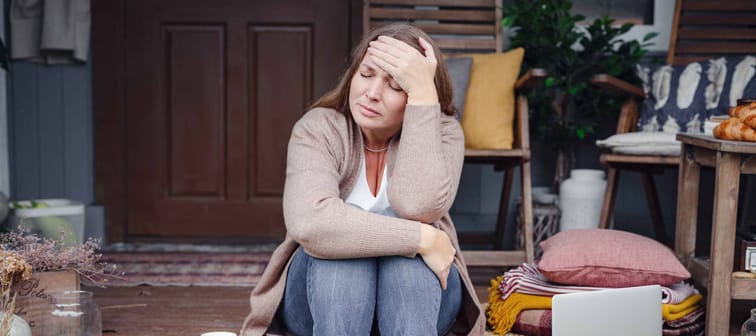 Caucasian woman upset on front porch, sitting with laptop