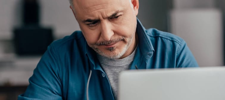 Middle aged man looking frustrated while working on his laptop holding glasses