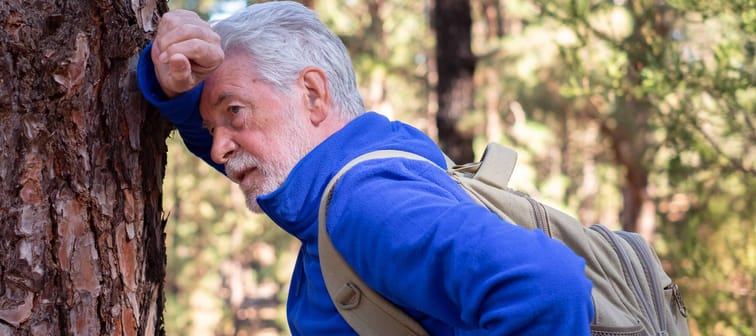 An older man takes a break while hiking in a forest.