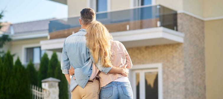 Older millennial Caucasian couple, backs to camera, looking up at a house