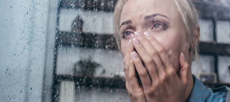 Woman crying in house looking at storm outside