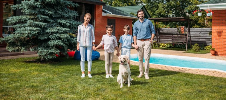 family with labrador dog looking at camera while holding hands on backyard of country house