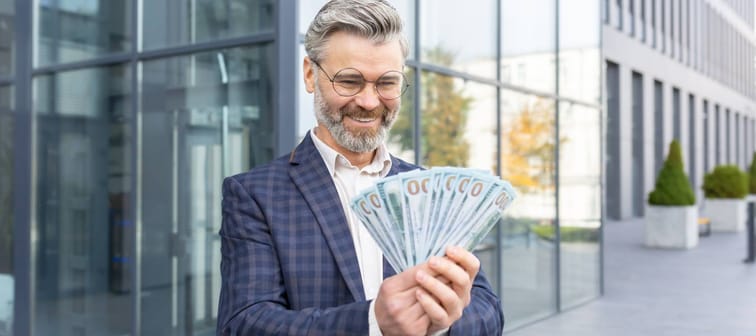 Incredibly happy businessman holds a stack of dollars in his hands, can't believe his luck, smiles