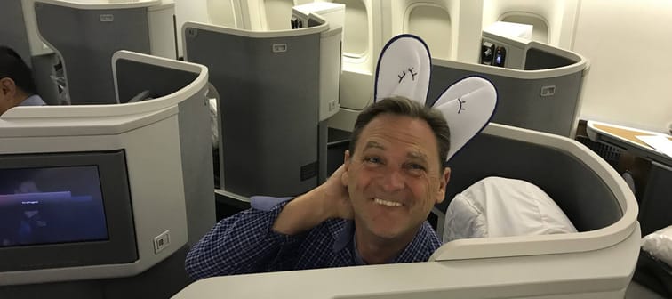 Man flying in first class and puts slippers on his head like a bunny and poses for the camera.