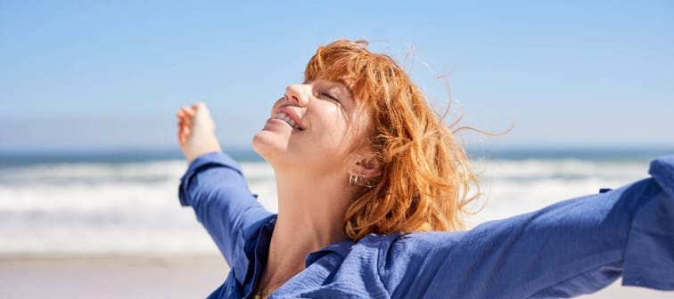 Portrait of healthy young woman standing on the beach with outstretched arms