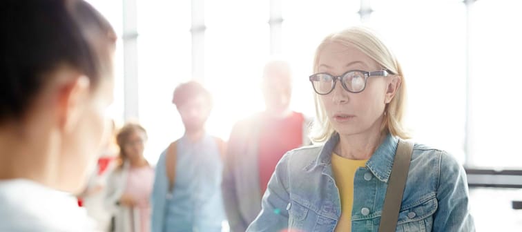 concerned senior Caucasian woman in casualwear and eyeglasses looking at bank teller