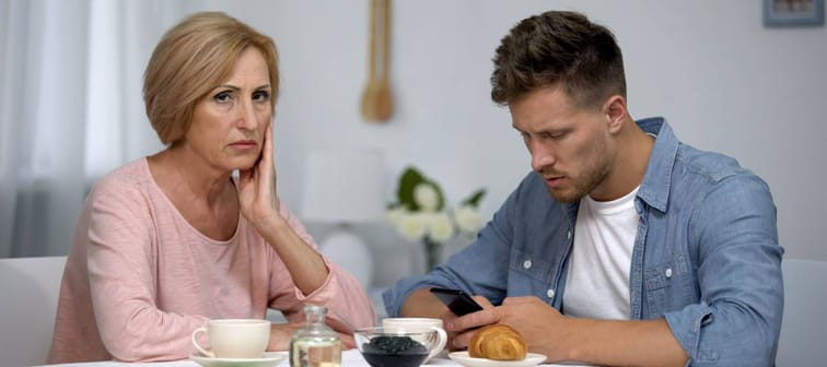 Mother worrying about adult son gadget addiction, male playing video game