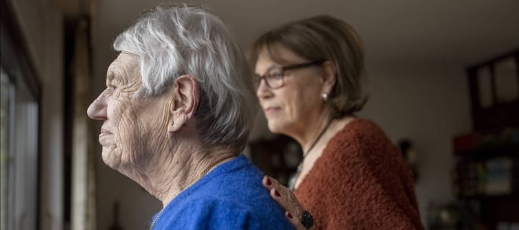 Elderly woman and senior woman standing and looking out a window