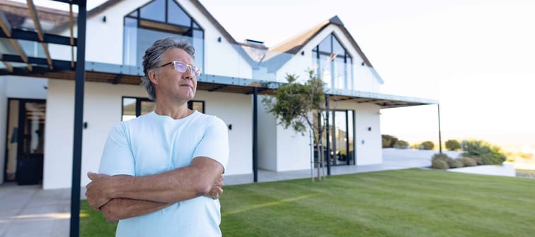 Caucasian senior man with arms crossed standing against nursing home in yard, copy space