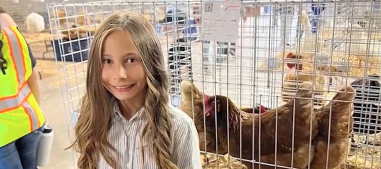 Young girl poses smiling in front of chicken cage.