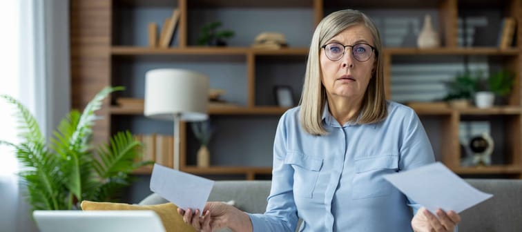 senior woman looking stressed and worried while holding bills