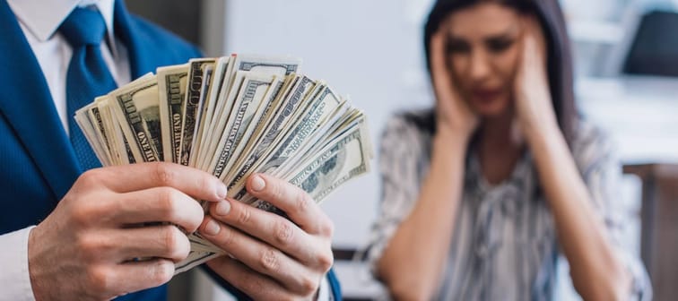 Man holding a fan of cash while wife sits in background