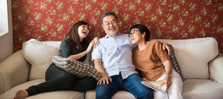 Family of three sitting on couch in living room, laughing together.