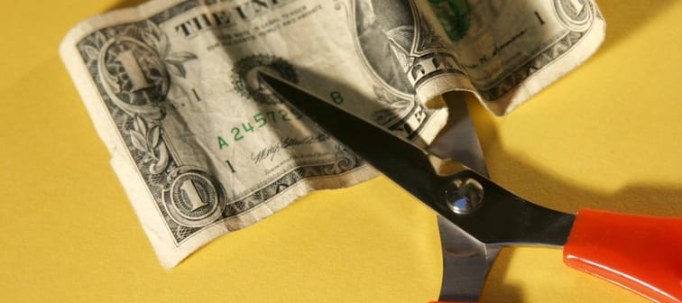 Red scissors cutting a U.S. dollar bill