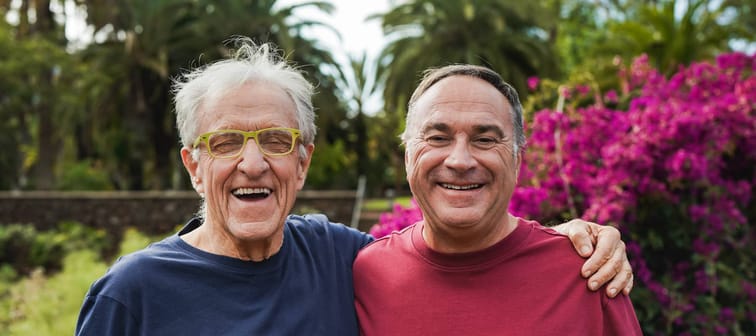 Senior men smiling on camera with their arms around each other's shoulders.