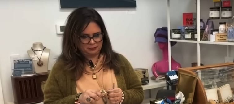 Woman works on making jewelry while standing behind counter in store.