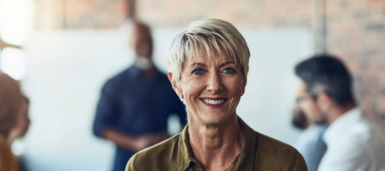 Mature businesswoman sitting in the boardroom during a presentation, smiling at the camera.