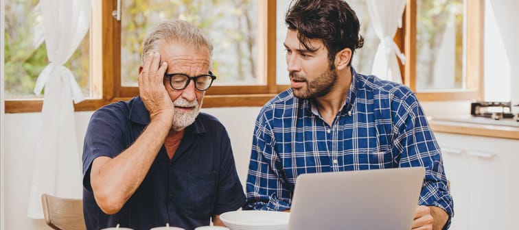 Senior man with adult son looking worried at a computer