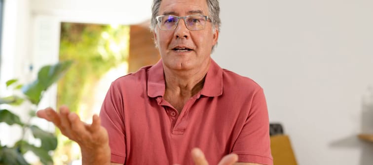 Man with grey hair gesturing at camera