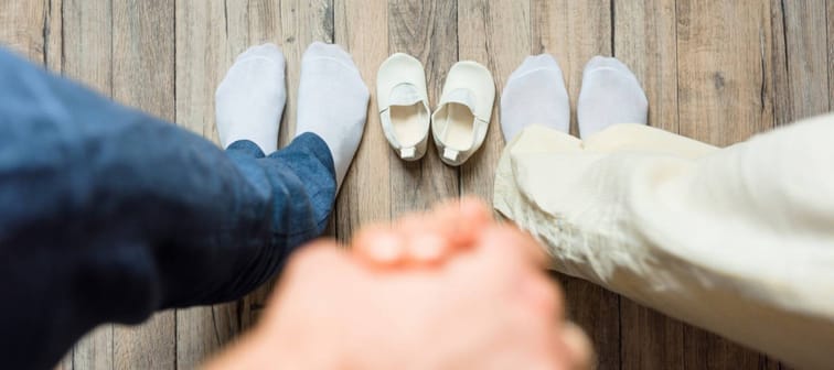 Feet of parents-to-be standing with baby shoes