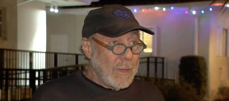 Man in baseball hat seen outside home at night, speaking to news camera.