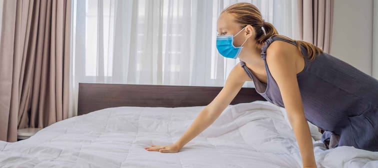 Young Female Housekeeper wearing a medical mask due to coronavirus quarantine COVID 19 Changing Bedding In Hotel Room