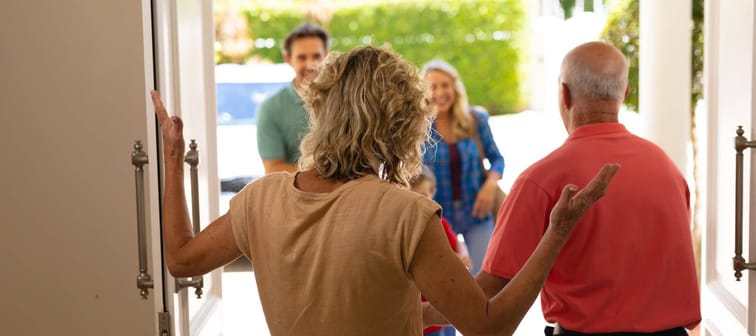 Rear view of senior couple welcoming their family at the entrance of the house