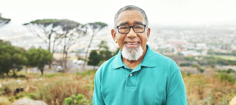 Older man smiles at camera while out on a hike.