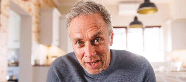 Man sits on couch, speaking on video call with very expressive face.