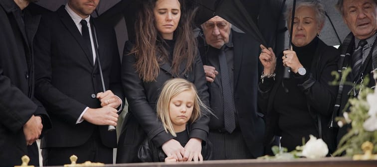 people at funeral with umbrella, flowers and coffin