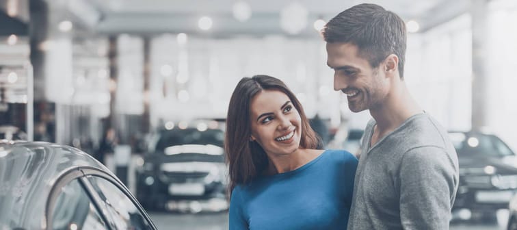 It is the one car I want! Beautiful young couple standing at the dealership choosing the car to buy