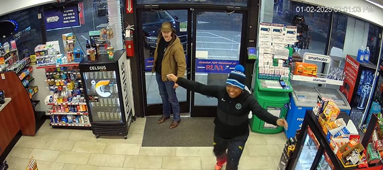 Still of gas station security camera footage, woman in winter hat with arms wide open, smiling.