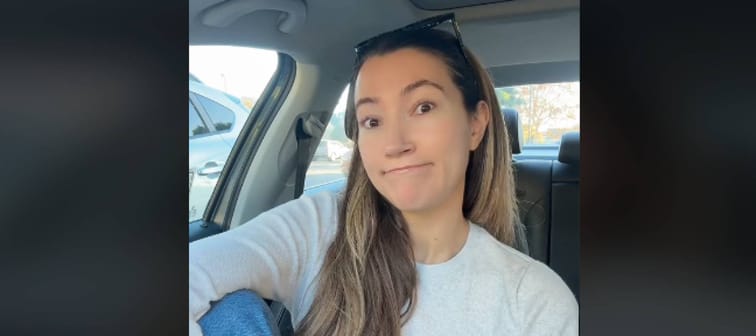 Woman sits in front seat of car, speaking directly to camera.