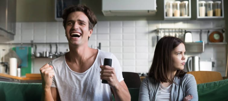 Angry woman sulking while excited football fan watching sport game holding remote