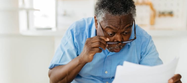 A man adjusts his glasses to read a bill.