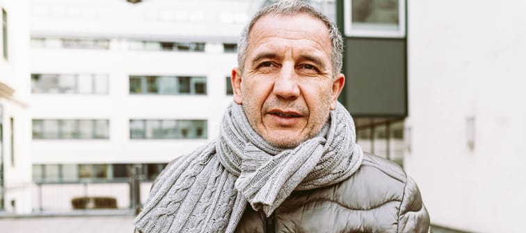 Man bundled up in winter clothing, seen outside, looking dismayed with hands in pockets.