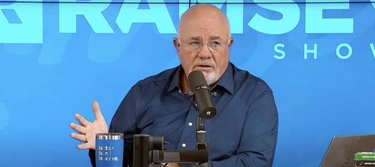 Dave Ramsey seen on set of his radio show, talking with one arm held out, fingers splayed.