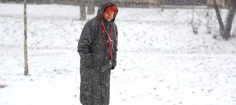 Senior woman walking on blizzard day in park. Weather changes concept.