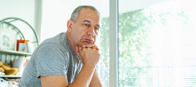 Sad middle-aged man at home sitting on bed in bedroom.