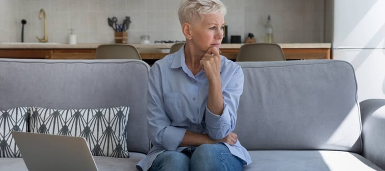 Concerned senior woman sits at table full of bills.