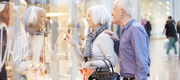 A senior couple point at items in a store window.