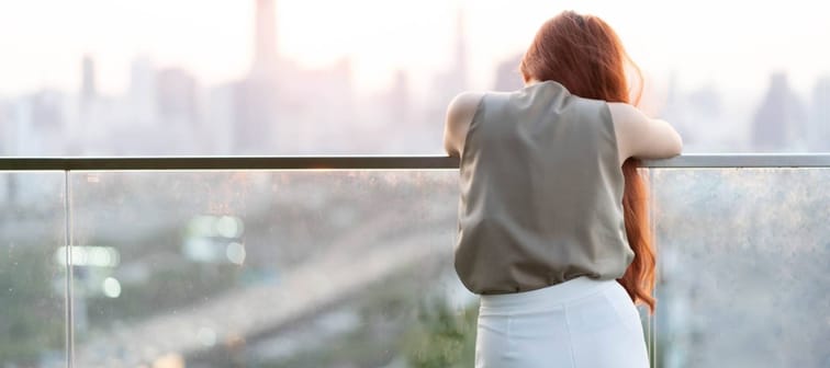 Woman leaning over a condo balcony overlooking a city.