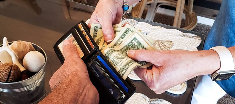 Woman's hand pulling American cash out of a man's wallet.