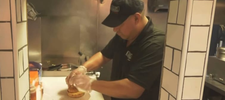 Man in deli kitchen, wrapping up bacon-egg-cheese sandwich.