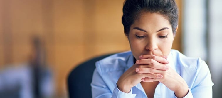 Woman clasped hands, thinking at a desk.