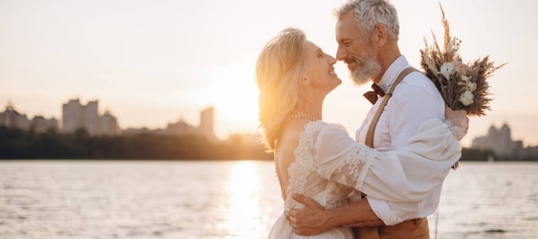 A bride and groom embrace on a beach.