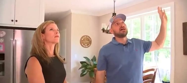 Man gestures with arm at ceiling, while he and woman beside him look up.